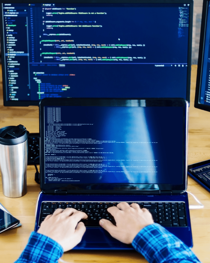 Person typing at a laptop with three screens behind them